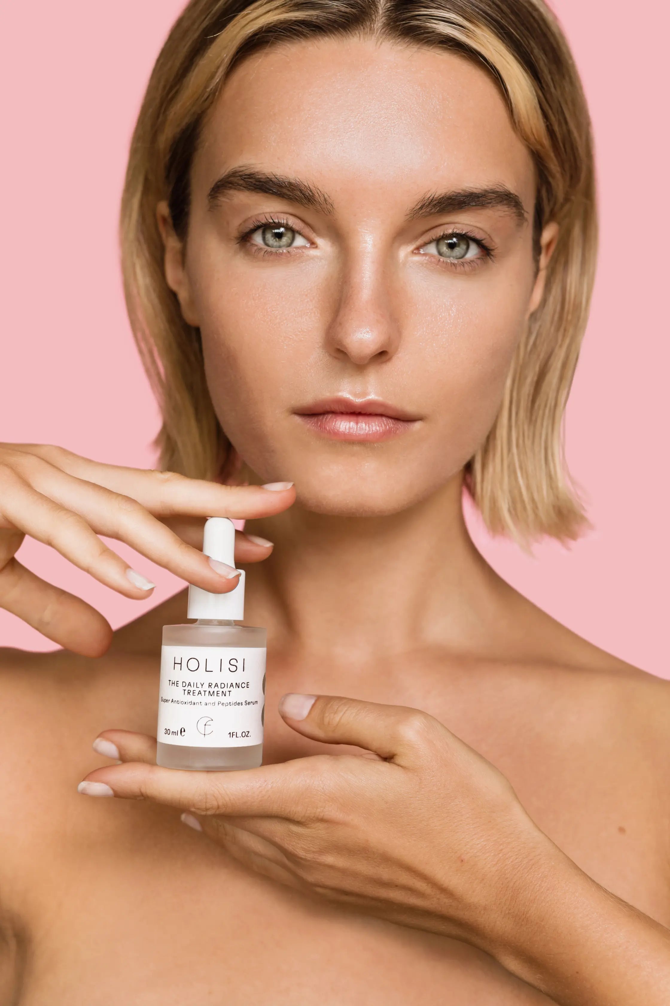 Frasco del sérum antioxidante The Daily Radiance Treatment de Holisi sobre la mano de modelo